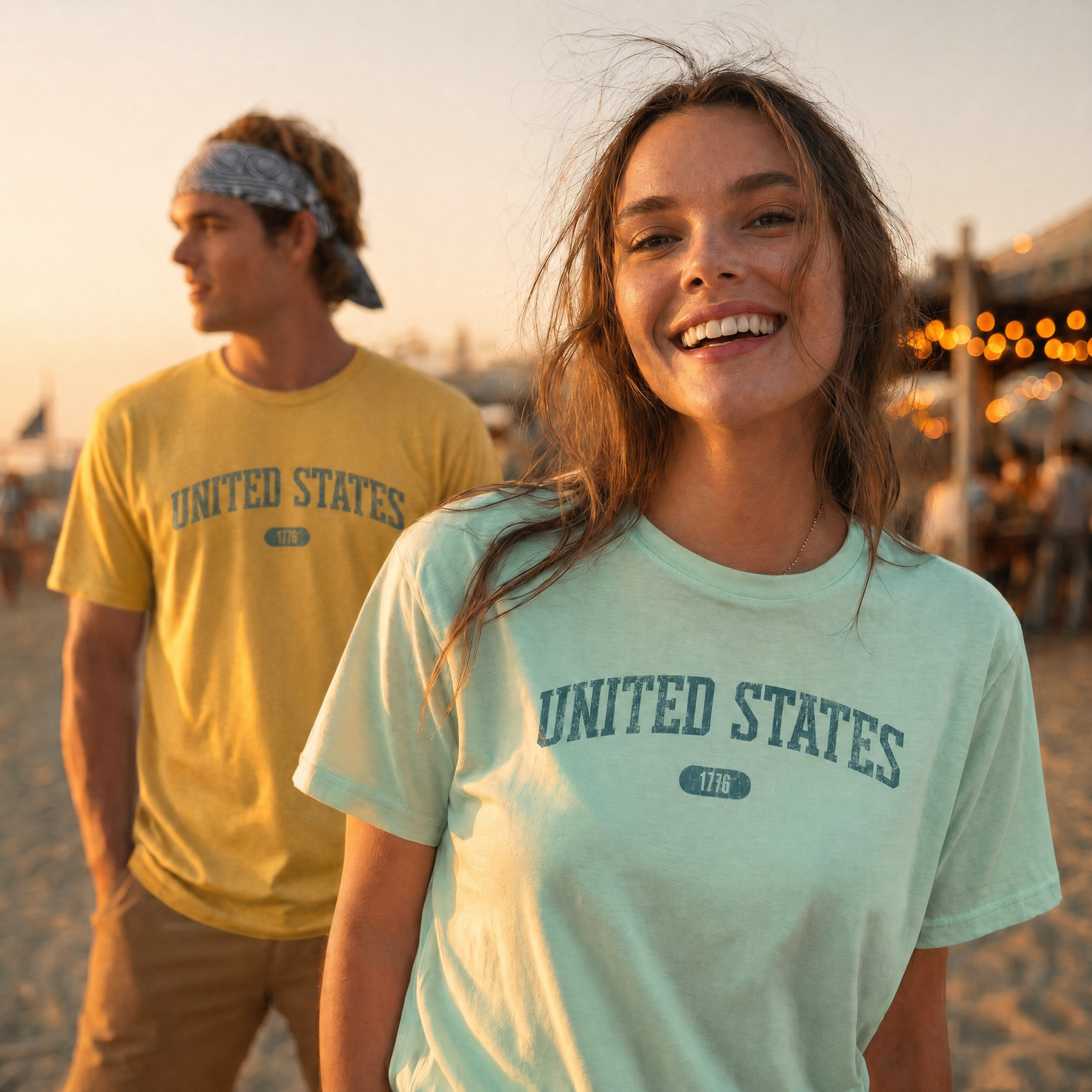 Woman and man wearing tees with 'UNITED STATES 1776' in teal collegiate text standing late in the day on a beach.