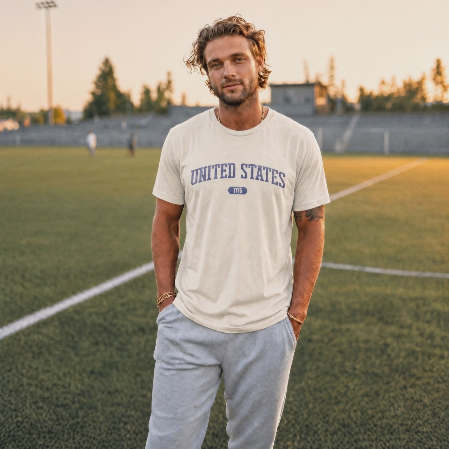 Video of a man wearing a natural t-shirt with 'UNITED STATES 1776' in blue collegiate text standing on a football pitch.