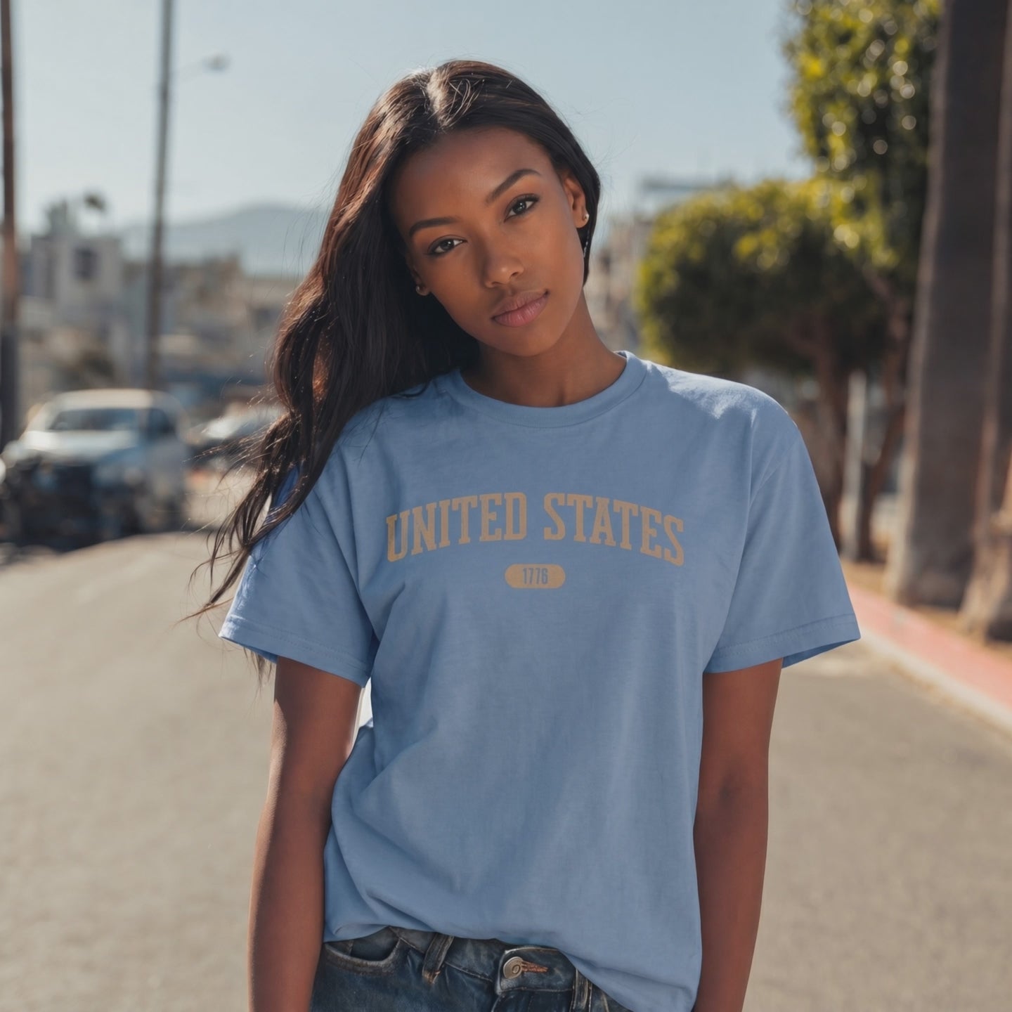 Video of a woman wearing a Steel Blue t-shirt with 'UNITED STATES 1776' in warm tan collegiate text.