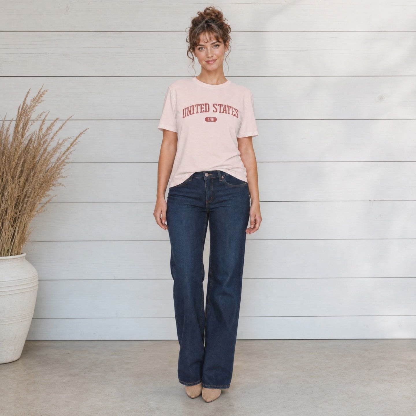 Video of a woman wearing a soft pink t-shirt with 'UNITED STATES 1776' in red collegiate text standing in a store studio.